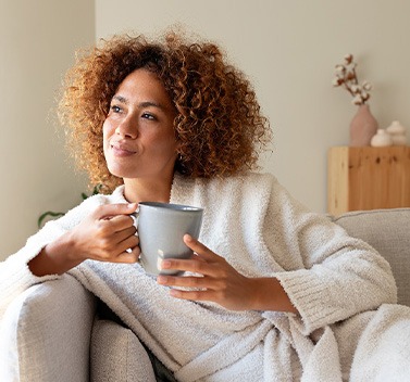 a woman holding a coffee mug and leaning over the arm of her couch