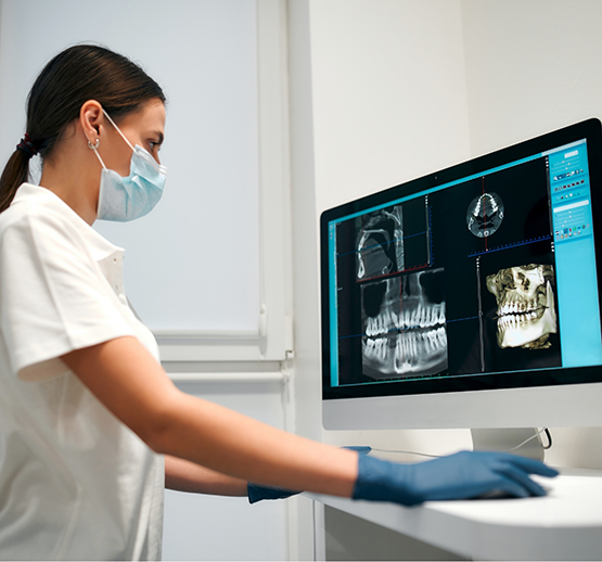 Female dentist with mask looking at dental X-rays on computer screen
