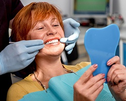 A mature woman admiring her dentures in a hand mirror