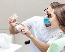 A dentist explaining how implants work by pointing to a jaw model