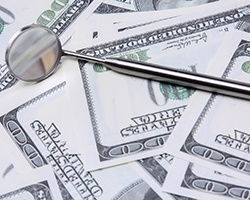 Dental tool on money representing the cost of dental emergencies