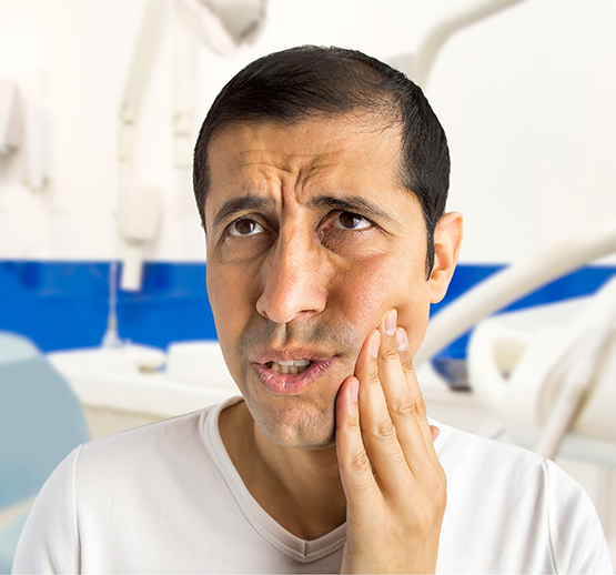 Man in white shirt rubbing jaw in pain in dental office