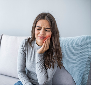 Woman in grey shirt sitting on couch with toothache