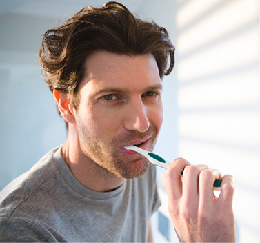 Man in grey shirt brushing his teeth