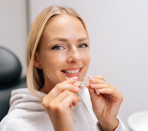 Closeup of woman smiling while holding clear aligner