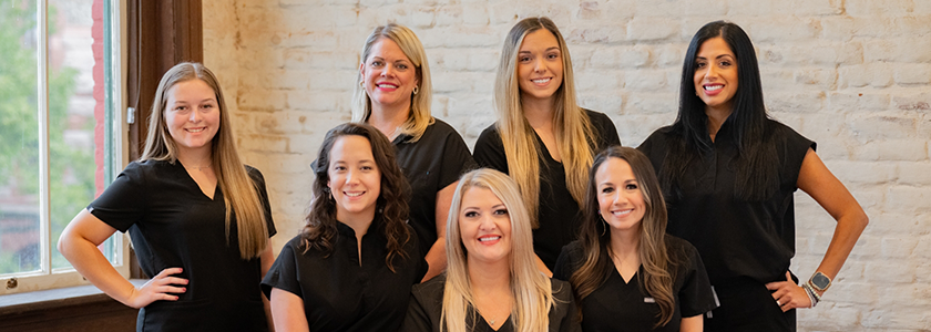 Dental team gathered in front of wall and smiling