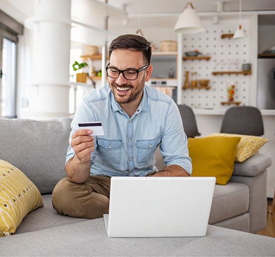 Man with glasses sitting at laptop and holding credit card