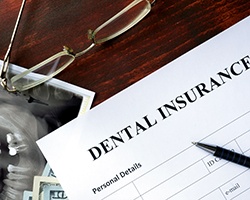 A dental insurance form set on a wooden desk next to glasses and X-rays