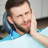 Man in dental chair holding cheek in pain