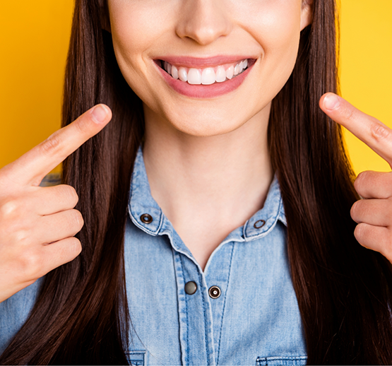 Woman in denim jacket pointing to smile