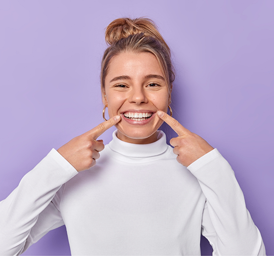 Woman in white sweater pointing to smile